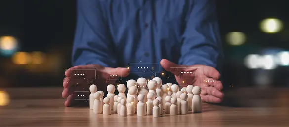 Hands gathered around a group of small wooden figures with speech bubbles