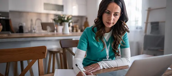 Nurse in scrubs studying at a laptop